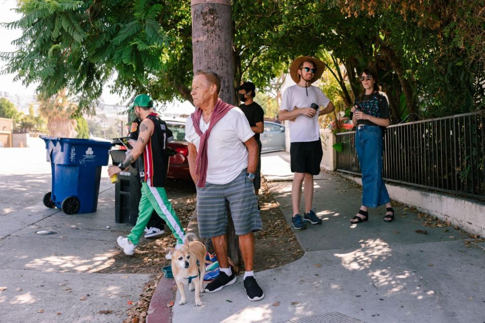 A man with a dog and others stand on a sidewalk