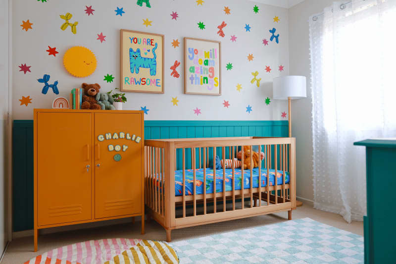 Nursery with teal and white walls, blue and white checkered rug, wood crib, and colorful painted wall mural