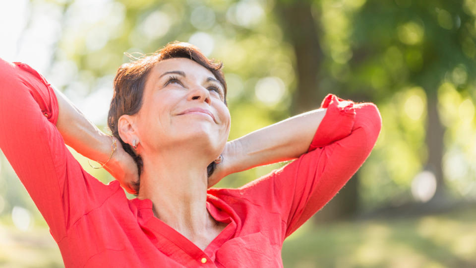 A woman with brown hair and a coral shirt with her sleeves rolled up looking toward the sun