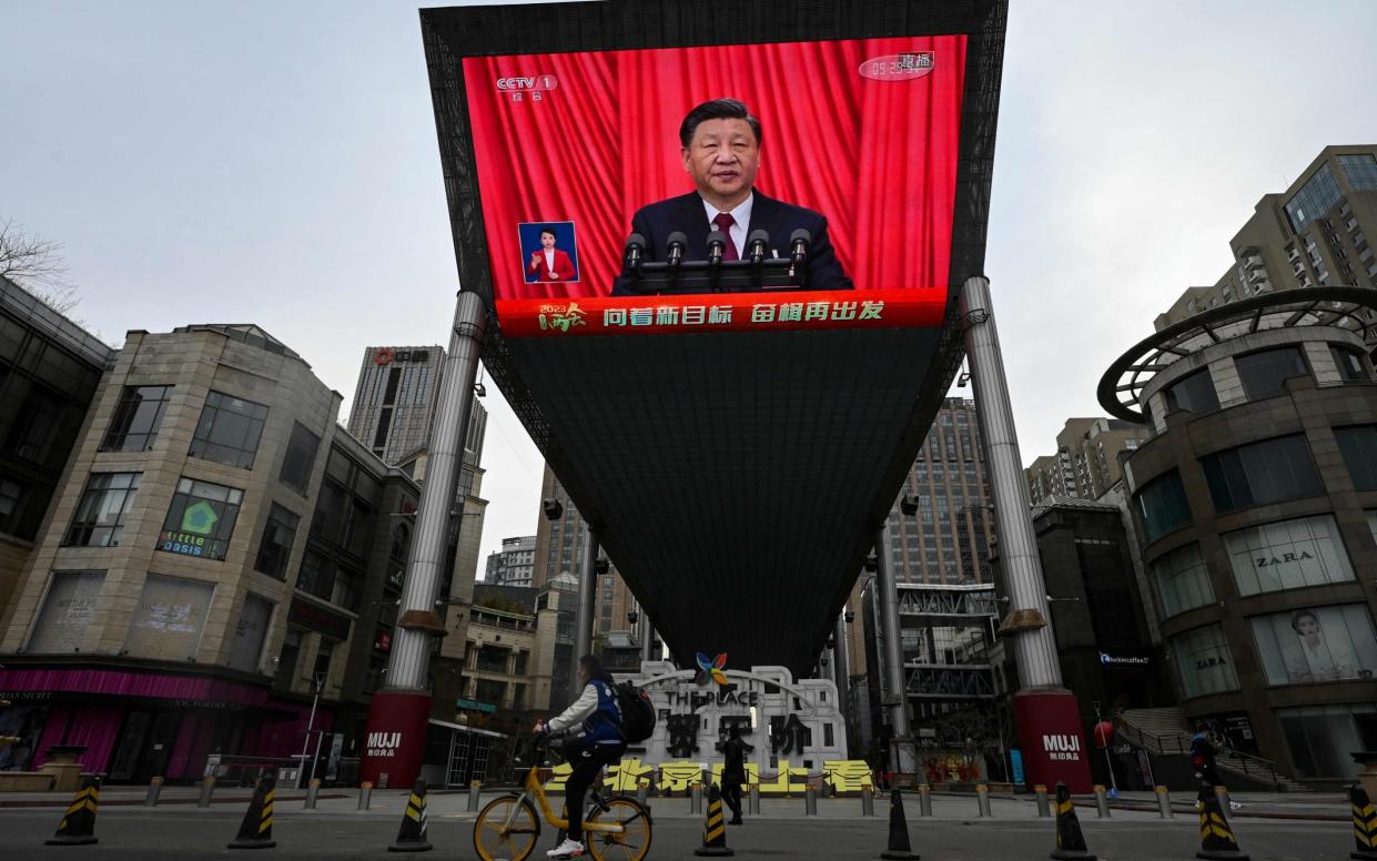 An outdoor screen shows live news coverage of Xi Jinping delivering a speech during the closing session of the National People's Congress (NPC) at the Great Hall of the People, along a street in Beijing - AFP