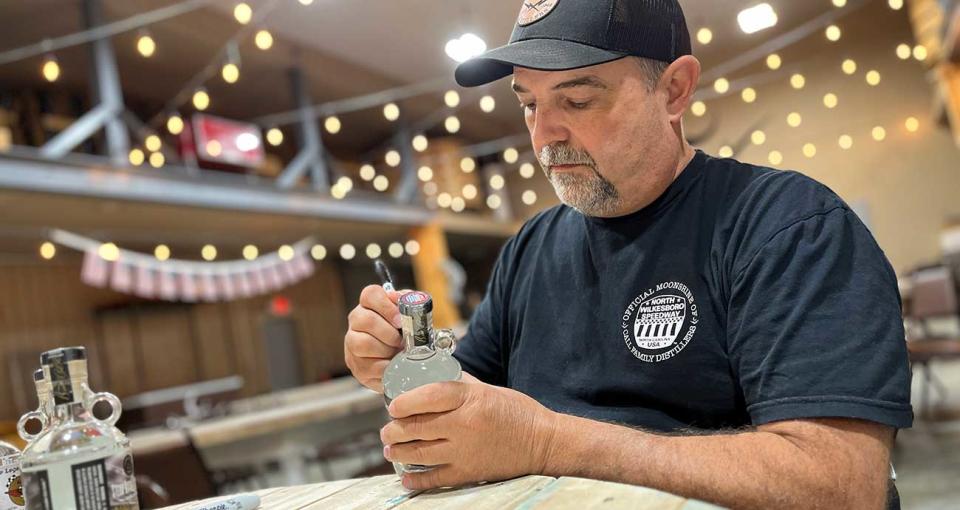 Moonshine maker Brian Call signs jars at Call Family Distillers.