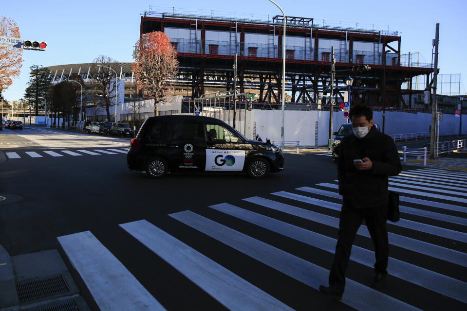 A man walks across a street as a massive steel structure of the TV Tower, that houses studios for live broadcasts of Tokyo 2020, in front of National Stadium, where opening ceremony and many other events are planned for postponed Tokyo 2020 Olympics, is seen from a rooftop observation deck Thursday, Jan. 21, 2021, in Tokyo. The postponed Tokyo Olympics are to open in just six months. Local organizers and the International Olympic Committee say they will go ahead on July 23. But it’s still unclear how this will happen with virus cases surging in Tokyo and elsewhere around the globe. (AP Photo/Kiichiro Sato)