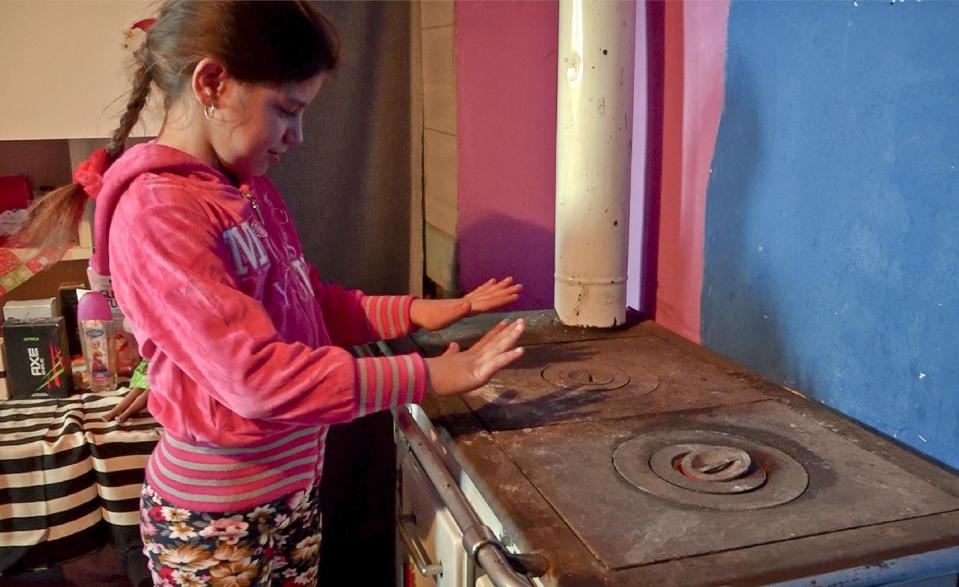 In this photo taken on Monday, Jan. 11, 2017, the sister of Ferenc Vadasz, name not available, warms her hands from the stove in the kitchen of their family home in Alsozsolca, Hungary. The big freeze that's keeping much of Europe in its grip is hitting hard impoverished communities, and particularly Roma, who are finding it hard to stay warm. (AP Photo/Andras Nagy)