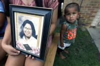 Kristina Taylor, 18, holds a portrait of her late mother, Sharon Taylor, while nephew Xavier Wishork, 2, stands at attention, Tuesday, July 22, 2020 in Tucker, Miss. For the Taylor family, June 2020 was supposed to be for celebrating daughter Kristina being selected as valedictorian at Choctaw Central High, the tribal high school for the Mississippi Band of Choctaw Indians. Instead, the family buried the mother, a victim of COVID-19. (AP Photo/Rogelio V. Solis)