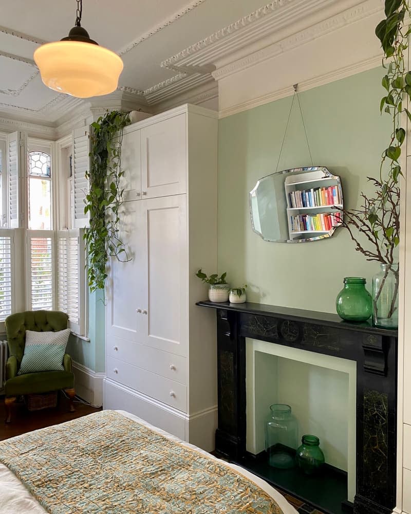 Mirror hanging over fireplace mantel in green painted bedroom.