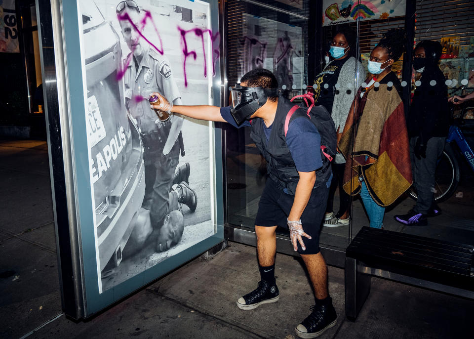 A demonstrator spray-paints a poster of Derek Chauvin’s knee on George Floyd’s neck on May 31. “Out of nowhere, this guy pulled out a purple spray can and just started writing on it. These ladies were walking by and paused to look at it. They were looking at it, like, Is this to attack us or to stop us from being silent?” | Malike Sidibe for TIME