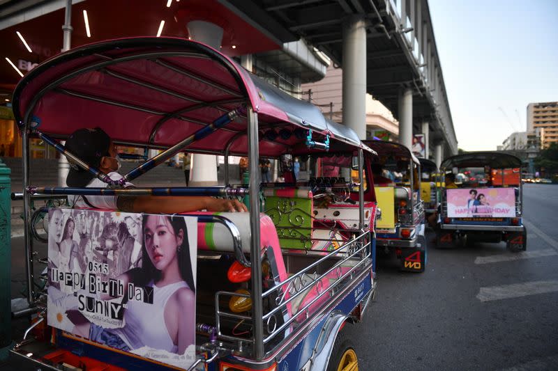 Tuk-tuk drivers, with their vehicles decorated with banners of K-pop stars, wait for customers in Bangkok