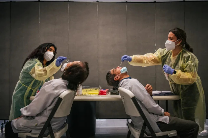 two people in masks give covid nasal tests to workers