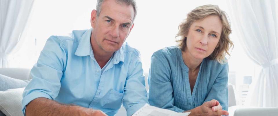 Worried couple paying their bills online with laptop looking at camera at home in the living room