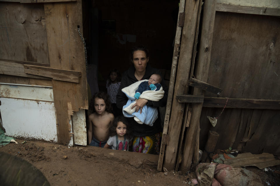 Pamela dos Santos Pereira, a 33-year-old mother of six children, stands in her home's doorway holding her one-month-old baby Joao, flanked by her 6-year-old son Issac and 4-year-old daughter Debora, in Brasiliandia, one of Sao Paulo's poorest neighborhoods, in Brazil, on Sept. 29, 2022. (AP Photo/Victor R. Caivano)