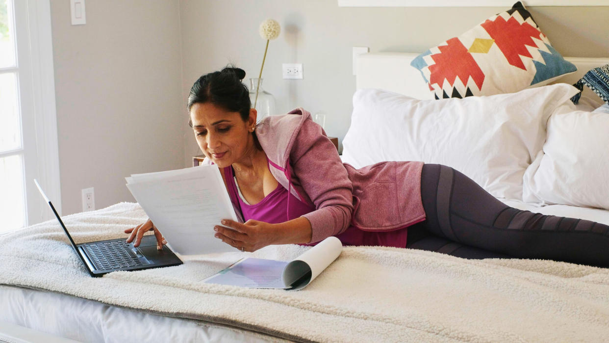 A mature aged woman working with a laptop computer in the bedroom of her suburban home in Los Angeles California USA.