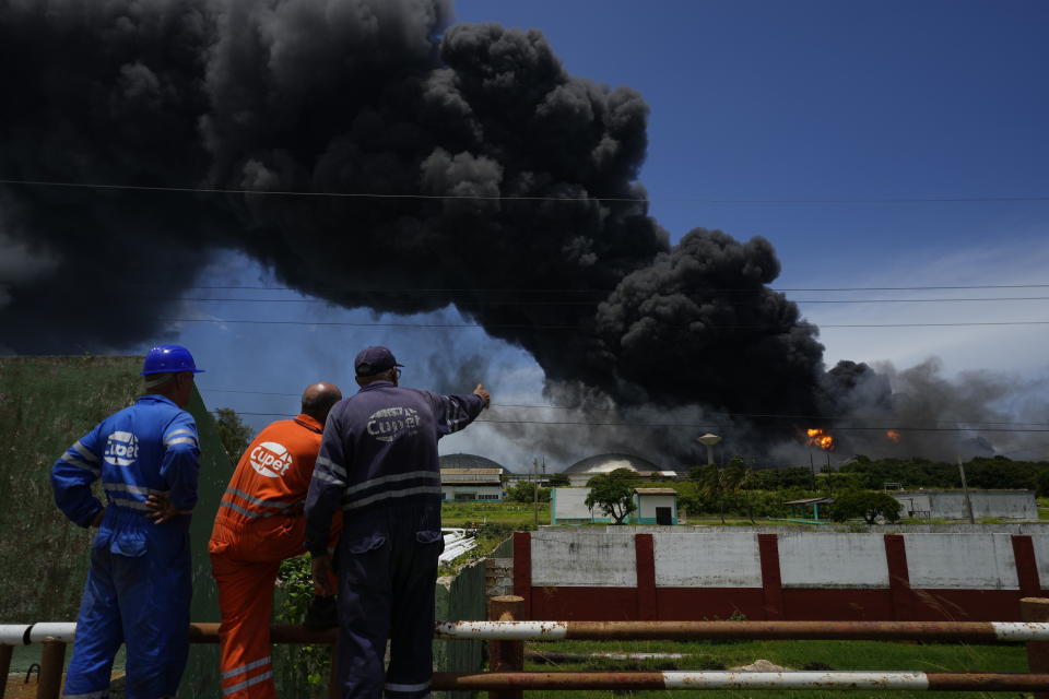 Los trabajadores del Sindicato Petrolero de Cuba observan una enorme columna de humo que se eleva desde la Base de Supertanqueros de Matanzas, mientras los bomberos trabajan para sofocar un incendio que comenzó durante una tormenta eléctrica la noche anterior, en Matazanas, Cuba, el sábado 6 de agosto de 2022. (AP Foto/Ramón Espinosa)