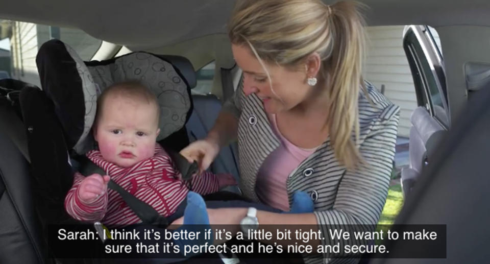 A mother buckling her child into a child car seat making sure the harness is tight