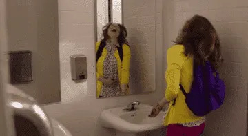 Kimmy Schmidt looking in a public bathroom mirror.