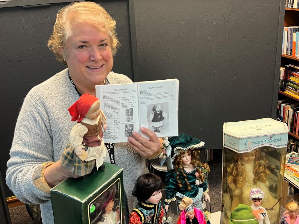 Carrie Cavanaugh, director of the Center for Active Adults in South Lyon, holds up a Russian doll and a collector's book. The doll is one of more than 300 the center is auctioning.