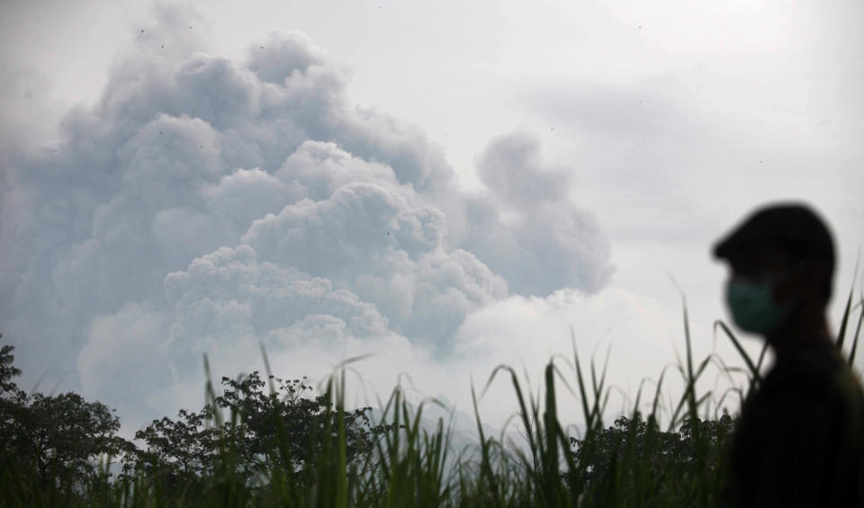 A man watches from Mbaladak village in Blitar, East Java, Indonesia, as Mount Kelud erupts Friday, Feb. 14, 2014. Volcanic ash from a major eruption in Indonesia shrouded a large swath of the country's most densely populated island on Friday, closed three international airports and sent thousands fleeing. (AP Photo/Trisnadi)