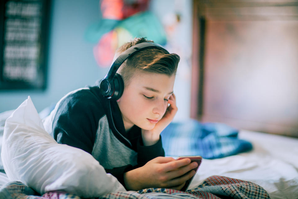 Person lying on a bed with headphones using a smartphone