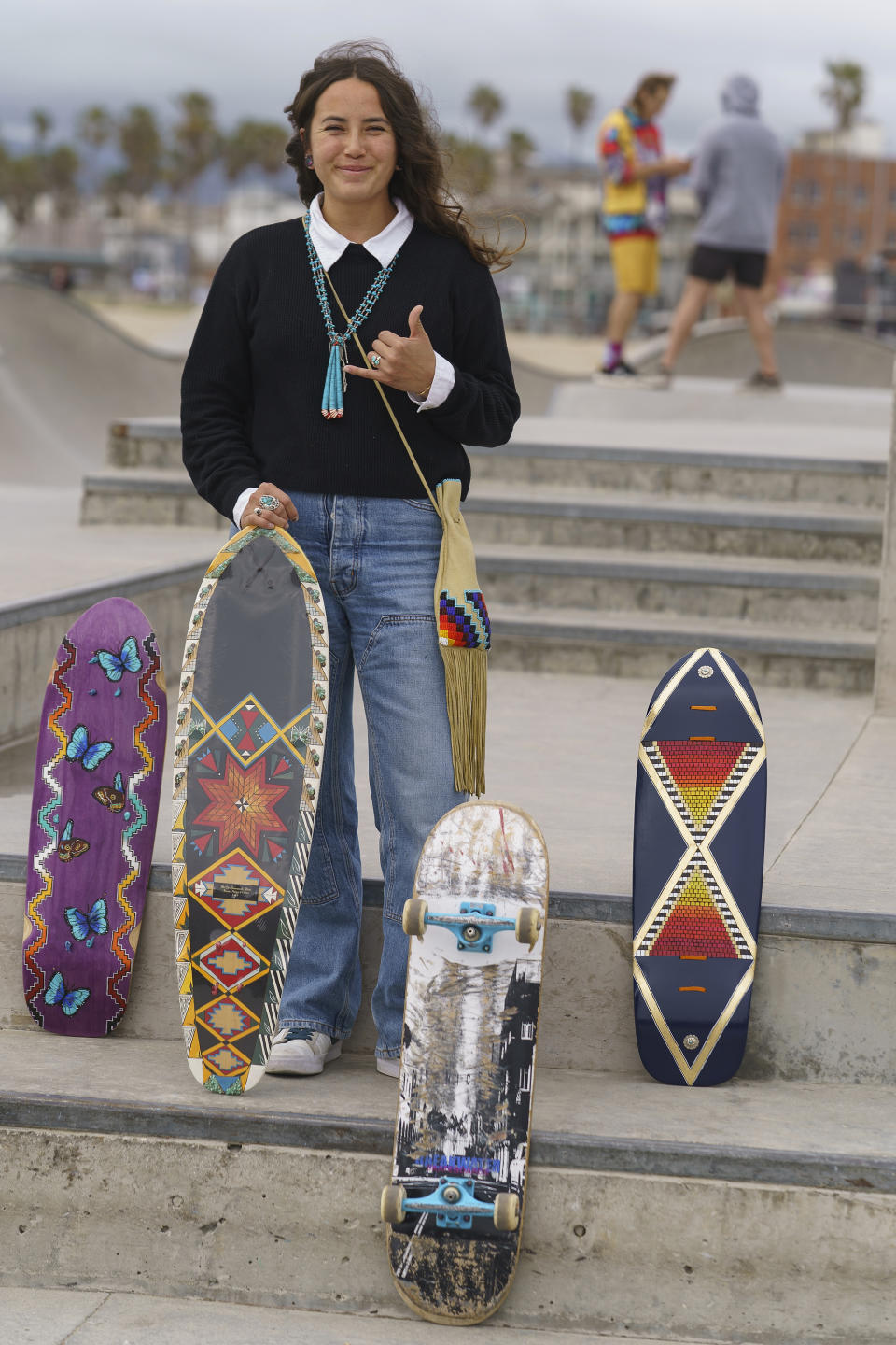 Expert skateboarder Di'Orr Greenwood, an artist born and raised in the Navajo Nation in Arizona and whose work is featured on the new U.S. stamps, poses for a picture with her painted skateboards in the Venice Beach neighborhood in Los Angeles Monday, March 20, 2023. On Friday, March 24, the U.S. Postal Service is debuting the "Art of the Skateboard," four stamps that will be the first to pay tribute to skateboarding. The stamps underscore how prevalent skateboarding has become, especially in Indian Country, where the demand for designated skate spots has only grown in recent years. (AP Photo/Damian Dovarganes)