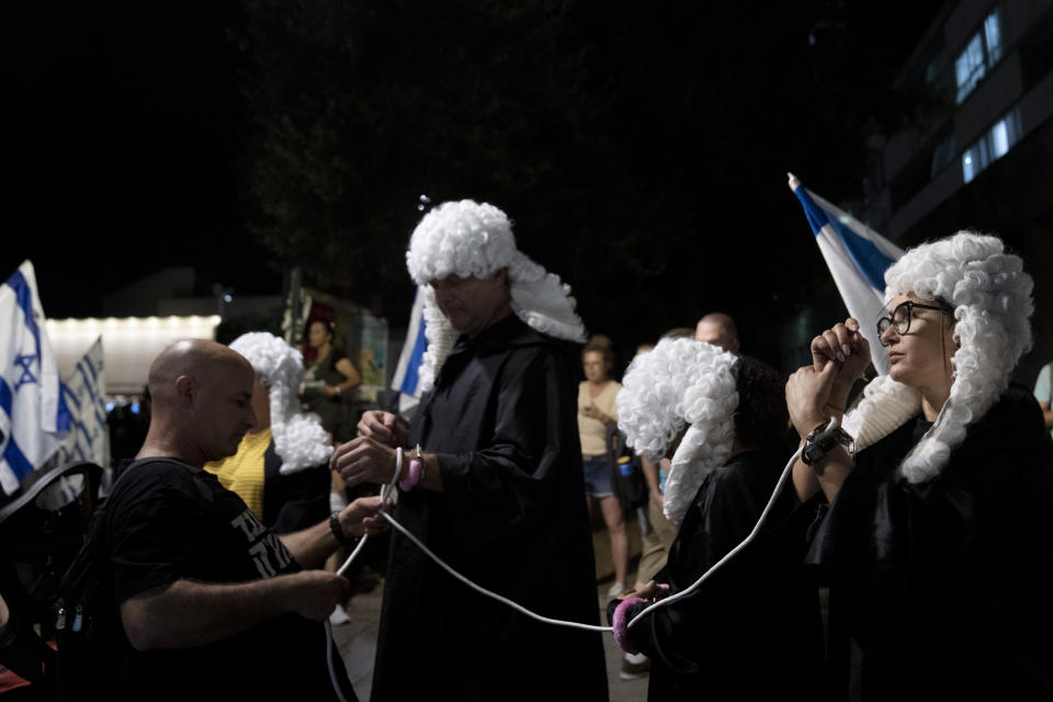 Israelis dressed as judges are tied together during a march in support of the judicial system during a protest against the plans by Prime Minister Benjamin Netanyahu's government to overhaul it, in Tel Aviv, Israel, Wednesday, Aug. 2, 2023. (AP Photo/Maya Alleruzzo)