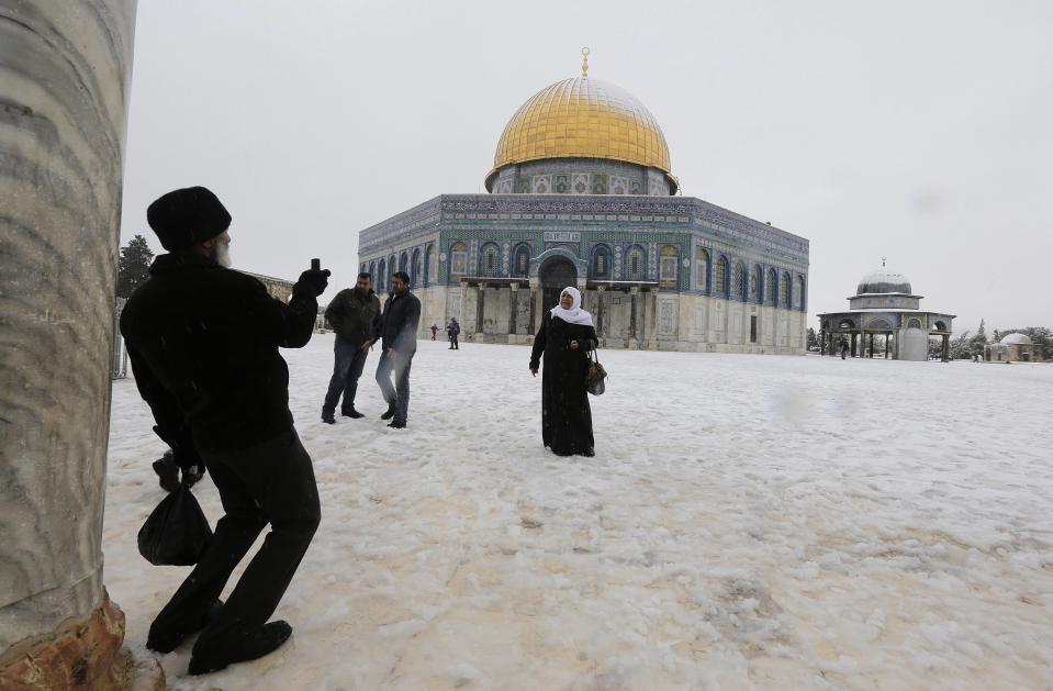 People have their pictures taken as snow falls in front of the Dome of the Rock in Jerusalem's Old City in winter