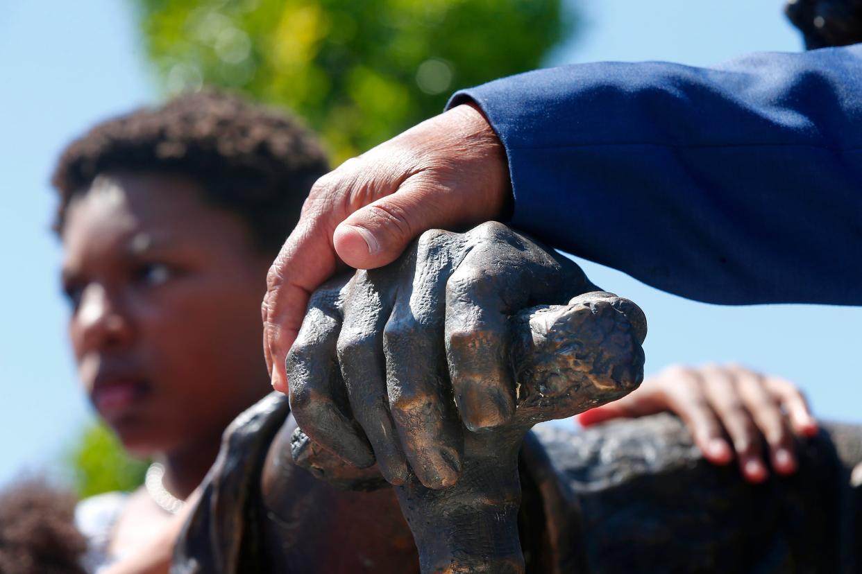 Richard Blake, sculptor, places his hand over the hand of the statue he made of Frederick Douglass, while in the background a boy holds the statue himself during the unveiling of the Douglass Memorial at the Abolition Row Park dedication in New Bedford.