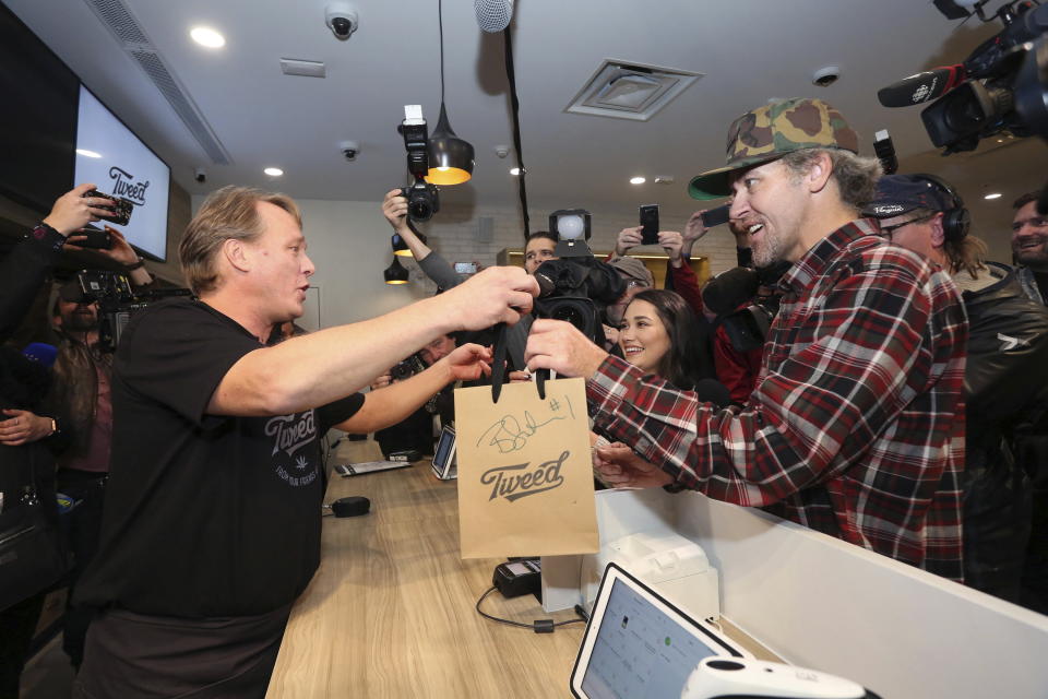 Canopy Growth CEO Bruce Linton, left to right, passes a bag with the first legal cannabis for recreation use sold in Canada to Nikki Rose and Ian Power at the Tweed shop on Water Street in St. John’s N.L. at 12:01 am NDT on Wednesday Oct. 17, 2018. (Paul Daly/The Canadian Press via AP)