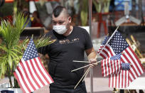 Marvin Turcios puts out American flags at Ocean's 10 restaurant on Miami Beach, Florida's famed Ocean Drive on South Beach, July 4, 2020. The Fourth of July holiday weekend began Saturday with some sobering numbers in the Sunshine State: Florida logged a record number of people testing positive for the coronavirus. (AP Photo/Wilfredo Lee)