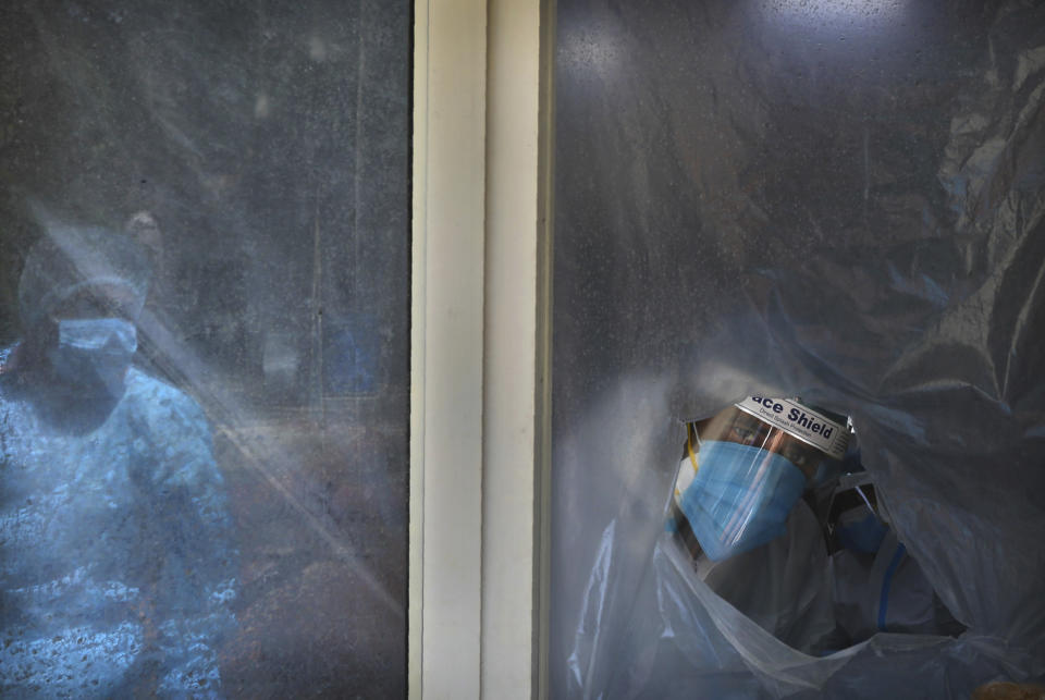 A health worker looks out from behind the plastic sheet covered window from where he conducts tests for COVID-19 in New Delhi, India, Saturday, Sept. 5, 2020. India's coronavirus cases have crossed 4 million, leading the world in new infections and deepening misery in the country's vast hinterlands where surges have crippled the underfunded health care system. Initially, the virus ravaged India's sprawling and densely populated cities. It has since stretched to almost every state, spreading through villages. (AP Photo/Manish Swarup)