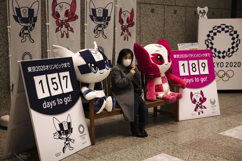 A woman removes her mask before taking pictures with the mascots of the Tokyo 2020 Olympics and Paralympics in Tokyo, Feb. 18, 2020. (AP Photo/Jae C. Hong, File)