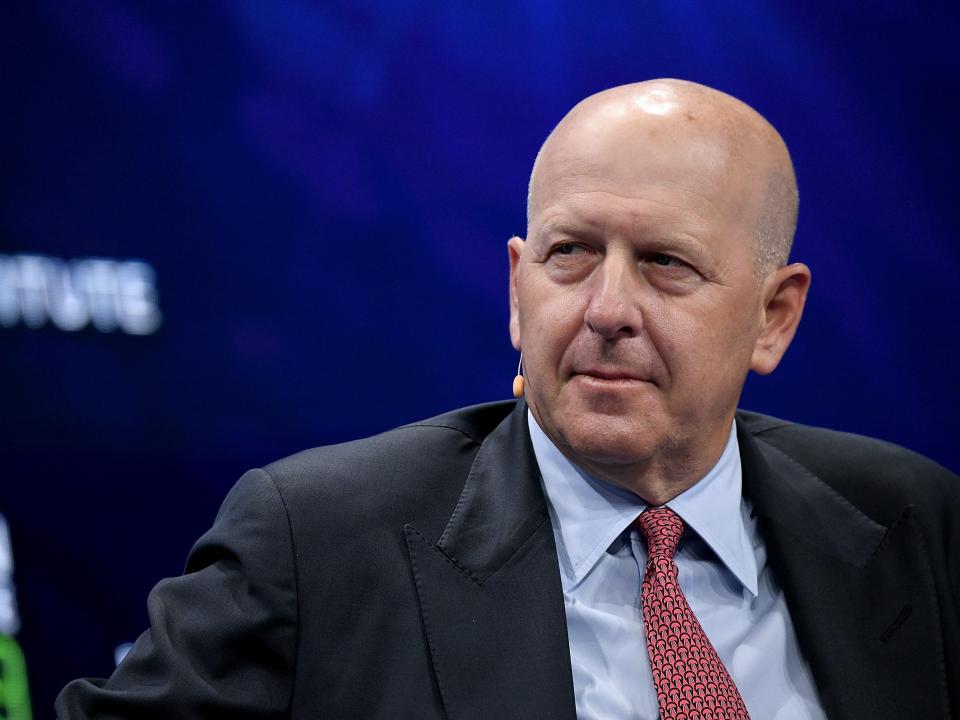 Goldman Sachs CEO David Solomon wears a pale blue shirt and red tie while speaking on stage.