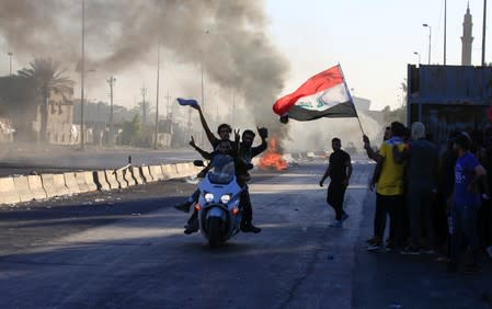 Demonstrators gesture as they ride a motorcycle at a protest during a curfew, three days after the nationwide anti-government protests turned violent, in Baghdad