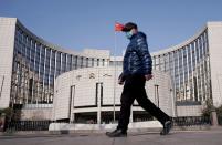 FILE PHOTO: Man wearing a mask walks past the headquarters of the People's Bank of China, the central bank, in Beijing