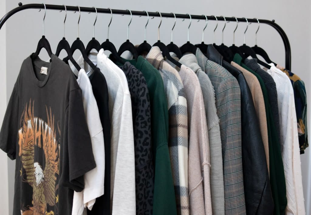 A capsule wardrobe sits on hangers on a clothing rack. 