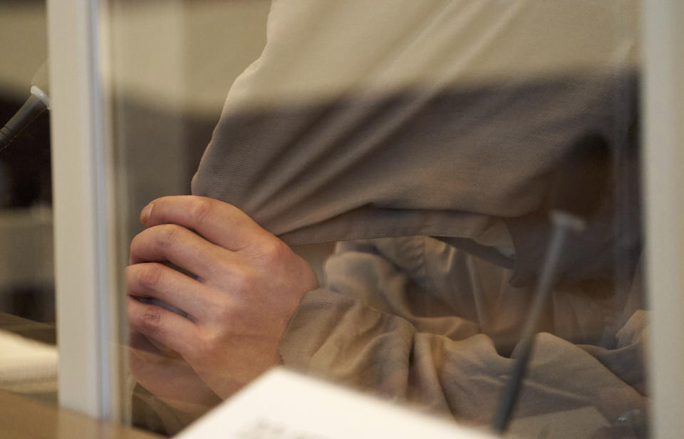 One of the defendants, Eyad A. (43), is sitting on the bench of the Higher Regional Court behind Corona protective screens, hiding his face under a hood in Koblenz, Germany, Thursday, April 23, 2020. Two former members of Syria's secret police go on trial Thursday in Germany accused of crimes against humanity for their role in a government-run detention center where large numbers of opposition protesters were tortured.(Thomas Frey/dpa via AP)