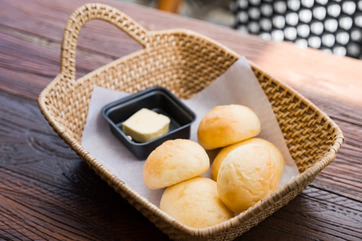 A basket with four bread rolls and a dish of butter on a wooden table