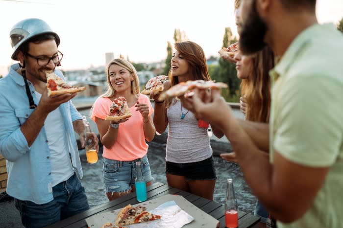 Young adults eating pizza at a picnic table.