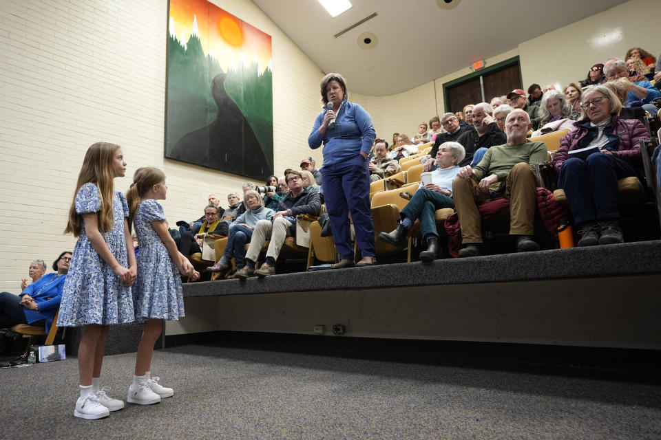 Former State Rep. Heidi Scheuermann, standing at center, speaks during a discussion about school board matters at the annual Town Meeting, Tuesday, March 5, 2024, in Stowe, Vt. The two girls at left wait to deliver the microphone to the next speaker. (AP Photo/Robert F. Bukaty)