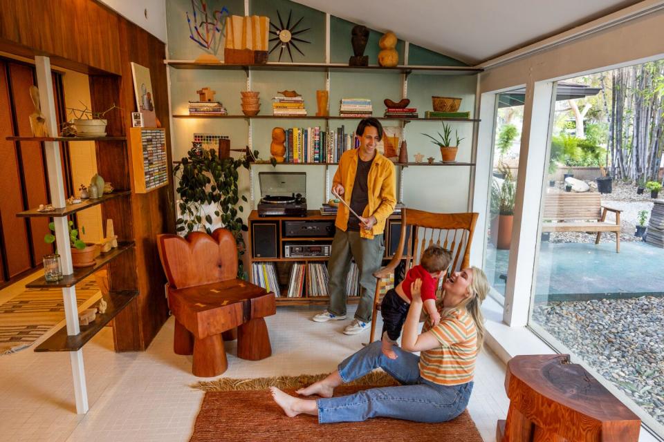 A man stands holding a record album next to a woman on the floor holding up a young boy