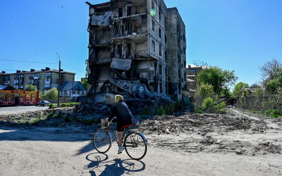 A woman rides a bicycle past an apartment building destroyed by the Russian army in the city of Borodyanka, northwest of the Ukrainian capital Kyiv - Sergei Chuzavkov/SOPA Images/Shutterstock/Shutterstock