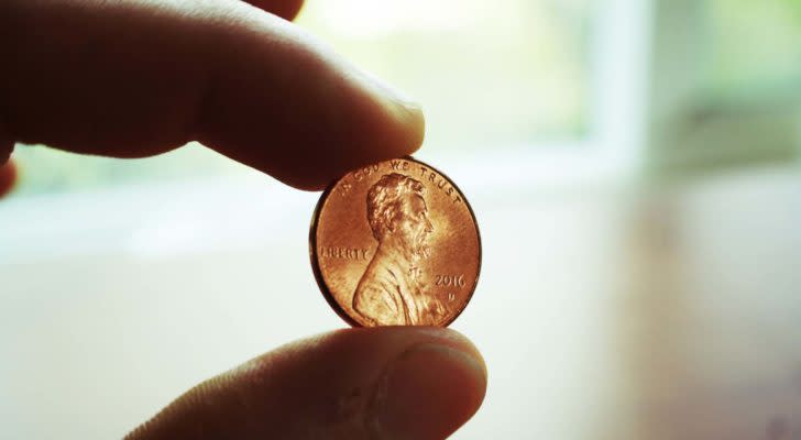 Image of a penny held between two fingers with a white indoor background. Dividend-Paying Penny Stocks