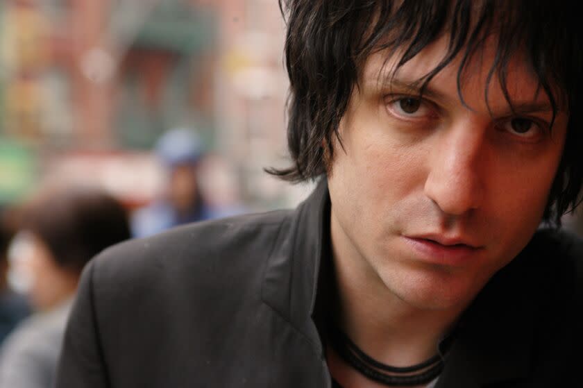 Jesse Malin is posing for a closeup photo wearing a grey blazer with his bangs flowing down his face