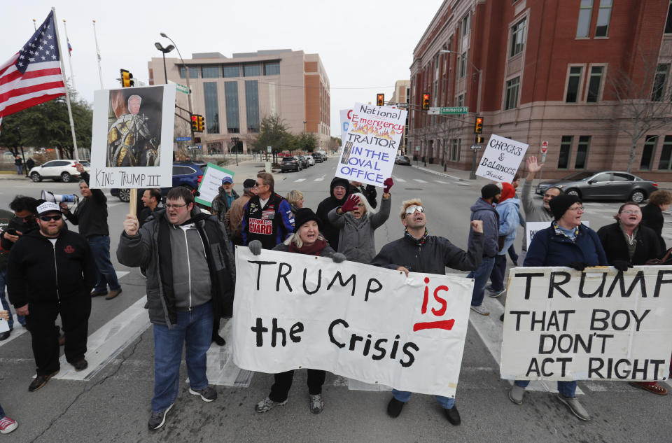 Protestors hold signs in a crosswalk in downtown Fort Worth, Texas, Monday, Feb. 18, 2019. People gathered on the Presidents Day holiday to protest President Donald Trump's recent national emergency declaration. (AP Photo/LM Otero)