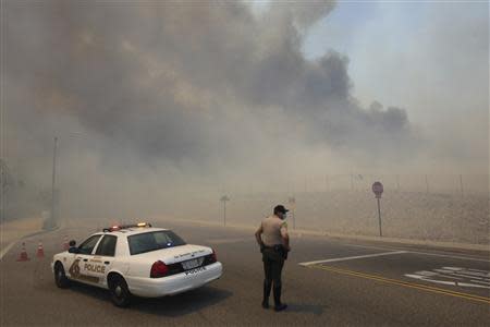 A police officer mans a roadblock as smoke billows from a wildfire driven by fierce Santa Ana winds in Rancho Cucamonga, California April 30, 2014. REUTERS/David McNew