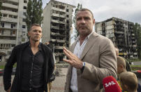 El exfutbolista y entrenador de la selección nacional de Ucrania, Andriy Shevchenko, izquierda, y el actor estadounidense Liev Schreiber hablan con medios de comunicación frente a un edificio destruido por la ofensiva rusa en Borodianka, cerca de Kiev, Ucrania, el 15 de agosto de 2022. (Foto AP/Evgeniy Maloletka)