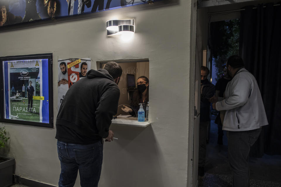 In this Tuesday June 2 , 2020, Katerina Dimitrakopoulou, second left, wearing a protective mask sits inside a ticket booth as she speaks with a moviegoer at the Panathinea outdoor cinema, in Neapoli, central Athens. (AP Photo/Petros Giannakouris)