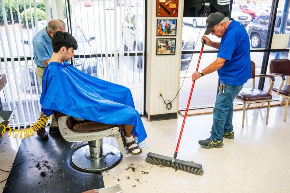 Jimmy Hill sweeps the floor while Gary Carter cuts Andrew Garcia’s hair inside Gary’s Barber and Style. Hill says he comes by every morning to take out the trash and sweep the floor to help out Carter.