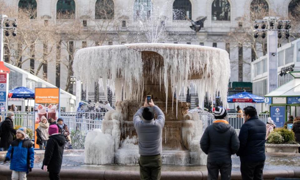 People take photos in front of a mostly frozen fountain in Bryant Park in New York City.