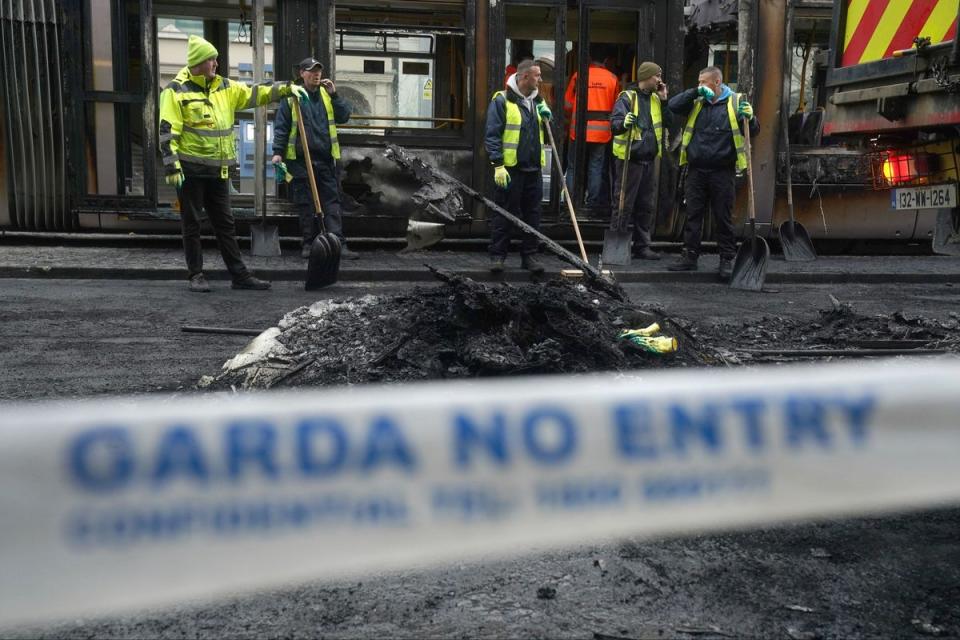Debris is cleared from a burned out Luas and bus on O'Connell Street in Dublin, in the aftermath of violent scenes (PA)