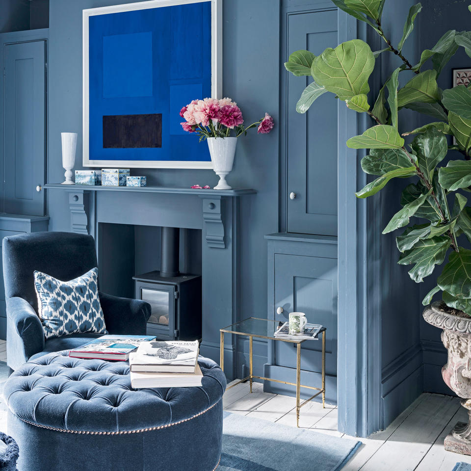 blue living room with artwork above fireplace, armchair and ottoman