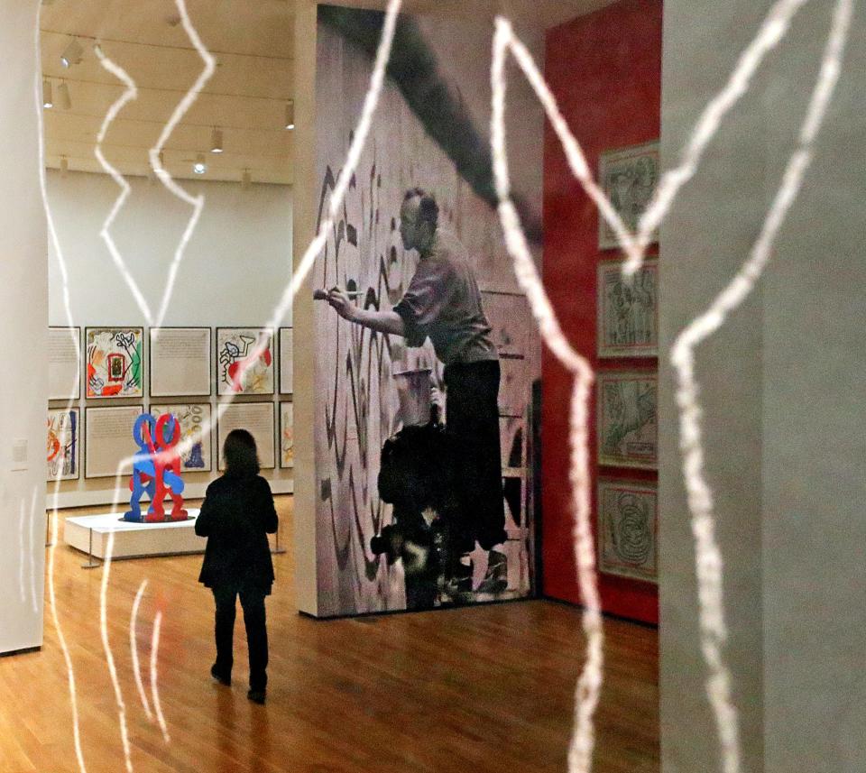 A museum guest and 1986 photograph of Keith Haring painting the Berlin Wall are reflected in an untitled subway drawing at the exhibit in Akron.